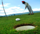 close up of golf hole and ball with golfer in the distance